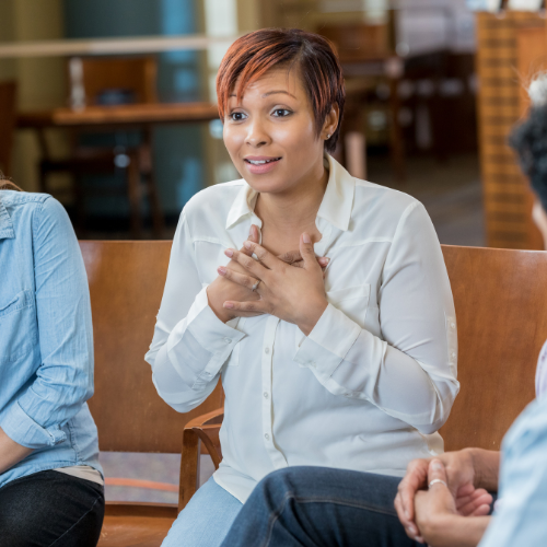 Group supervision in Portland Oregon, black woman with hands on heart, sitting on midcentury modern wooden chair in a circular group setting